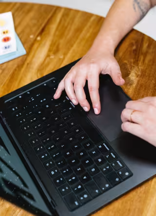 Handen van een designer werkend op een laptop aan een houten tafel