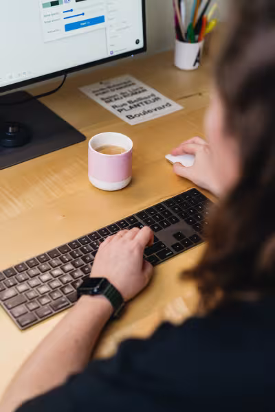 Janne Degryse, grafisch designer bij Studio Modular, werkend aan haar bureau met een iMac, toetsenbord en een roze koffiekopje